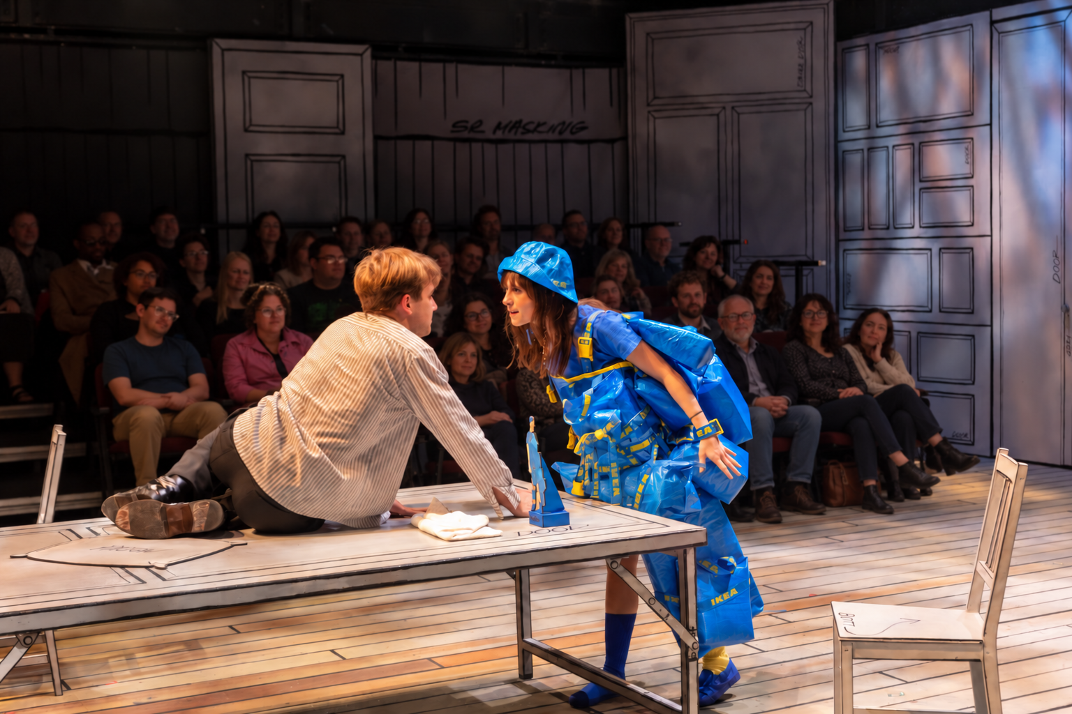 Two performers meet across a table before the audience.