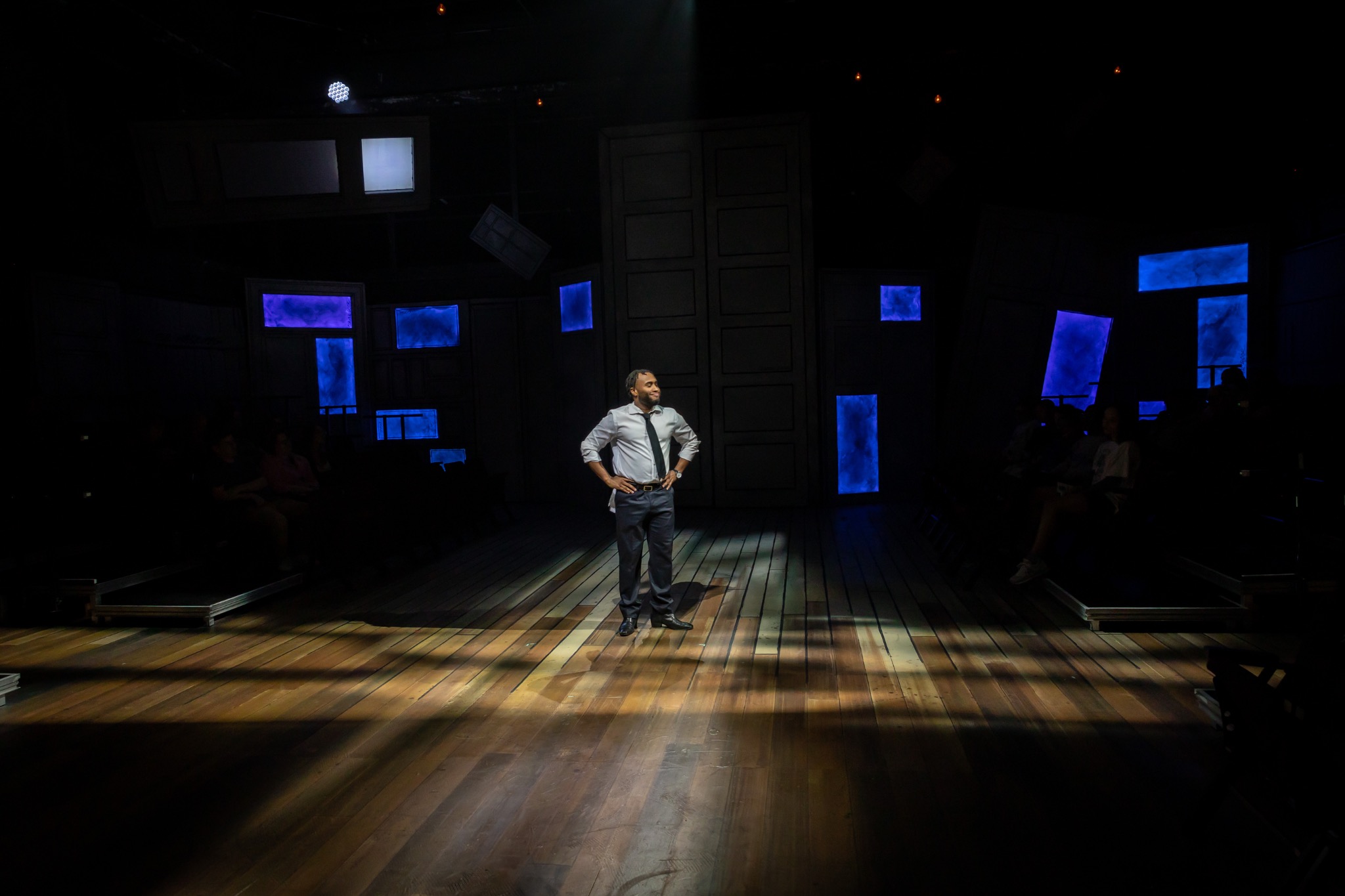 A lone performer stands under a spotlight in the blackbox.