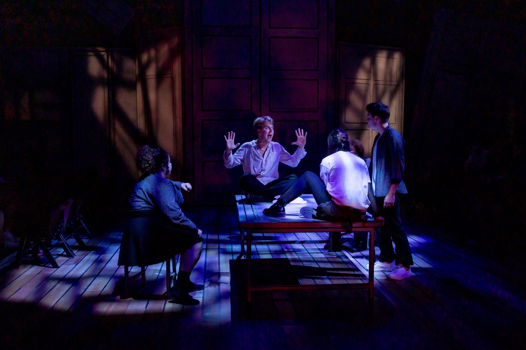 The ensemble surrounds a figure on a table under blue light.