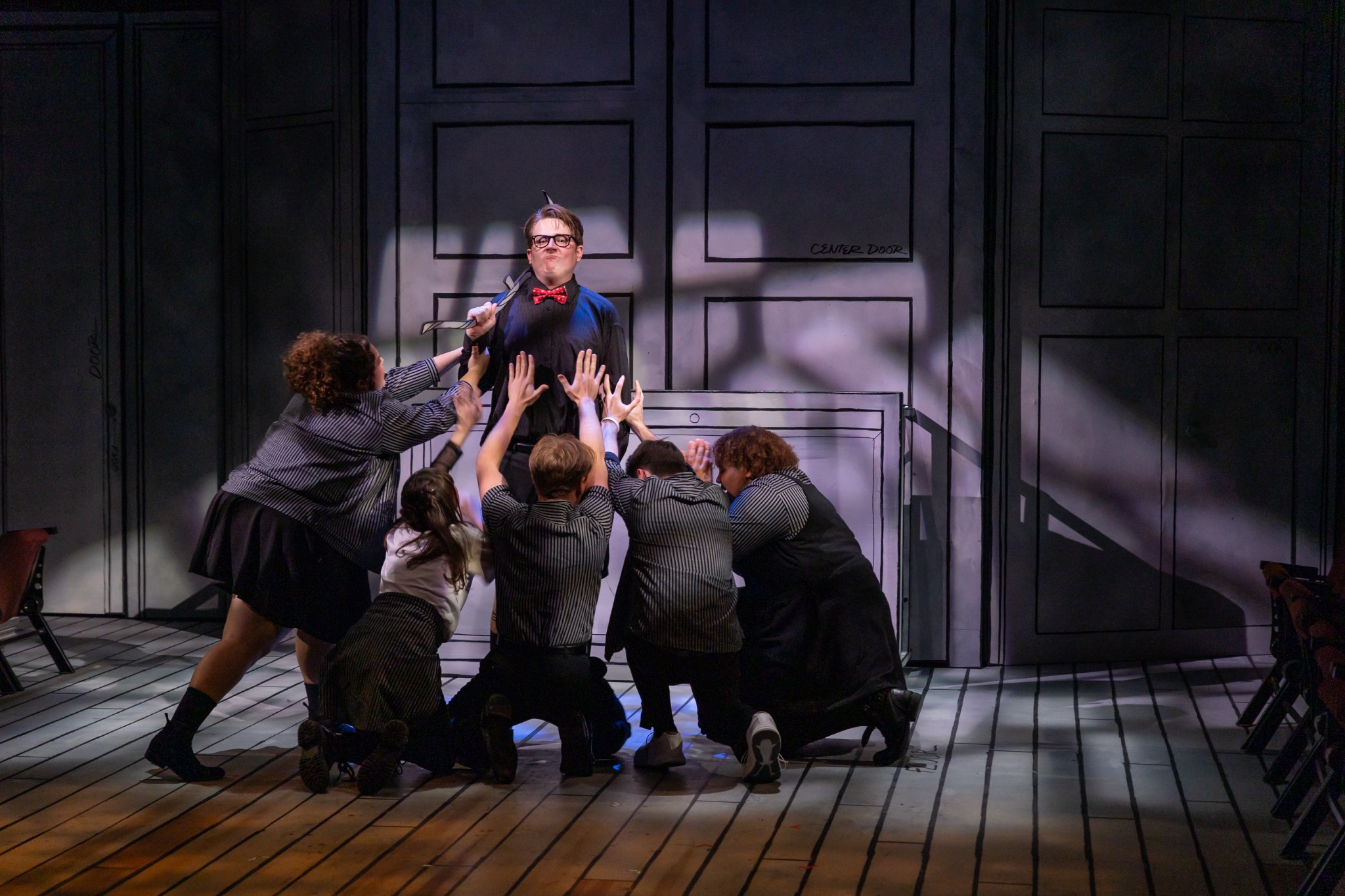 The ensemble reaches toward a performer before the scenic doors.